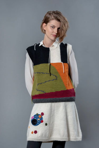 Woman wearing white wool knee length skirt and wool vest. The skirt has colourful bubble-like embroideries on the right leg.